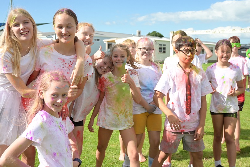 image shows group of children who have taken part in a school fun colour run they are smiling and covered in colour powder