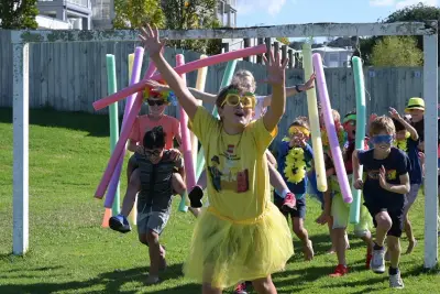 image shows picture of children taking part in a school fun run on a field. They are wearing colourful clothing.